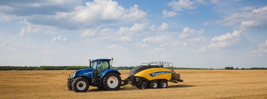 Ciągnik New Holland z prasą zwijającą na polu po żniwach