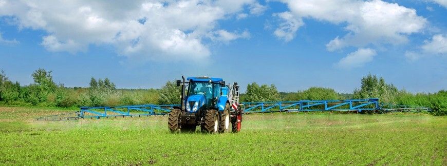 nowoczesny niebieski traktor z opryskiwaczem wykonujący oprysk pola