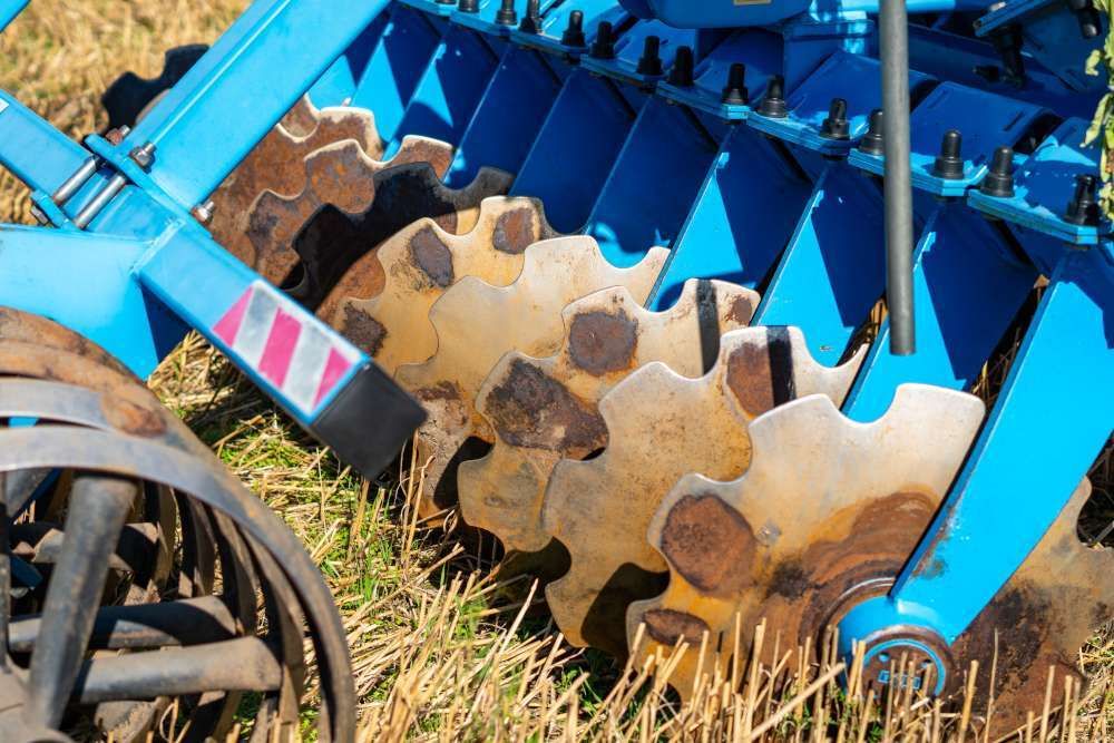 Zbliżenie na zębate talerze robocze niebieskiej brony talerzowej na ściernisku. Fot. Adam Bartosik - shutterstock.com